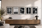Five black and white printable photography prints from the Timeless Fine Art Wall Art Bundle displayed above a modern wooden media console in a stylish contemporary living room with minimalist decor.