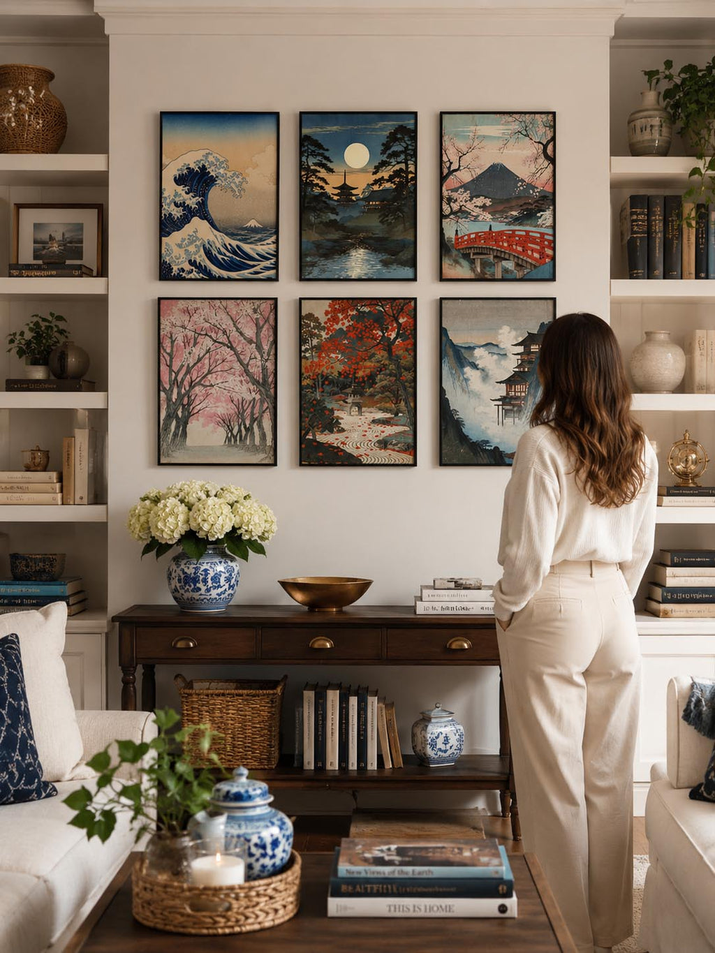 Vintage Traditional Japanese Vertical Set of 9 iArt Tech Studio displayed as a stunning 2x3 gallery wall in a bright American living room with built-in bookshelves, elegant wood console table and modern décor. Six vintage Japanese printable wall art prints in black frames create a sophisticated Japandi gallery wall above a console between decorative shelves, styled with luxury home accessories, natural lighting and a woman admiring the artwork. Perfect Japanese wall decor inspiration for living room, librar