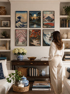 Vintage Traditional Japanese Vertical Set of 9 iArt Tech Studio displayed as a stunning 2x3 gallery wall in a bright American living room with built-in bookshelves, elegant wood console table and modern décor. Six vintage Japanese printable wall art prints in black frames create a sophisticated Japandi gallery wall above a console between decorative shelves, styled with luxury home accessories, natural lighting and a woman admiring the artwork. Perfect Japanese wall decor inspiration for living room, librar